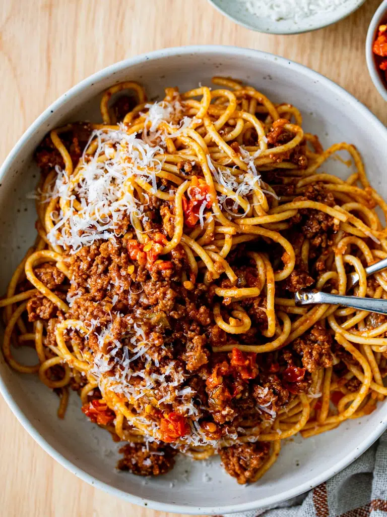 Close-up of Bolognese sauce with a fork and red chilli beside the plate.
