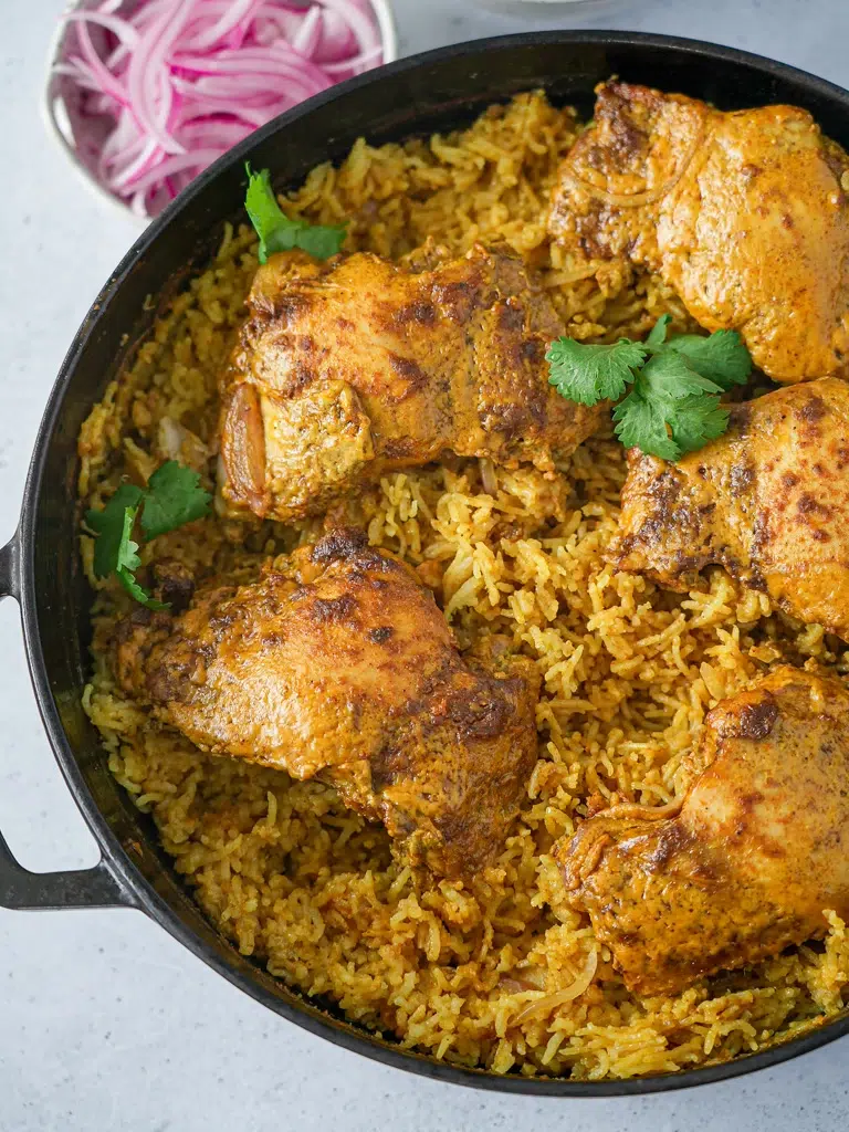 Overhead view of Chicken Korma Bake in a pan, featuring tender chicken pieces in a creamy sauce garnished with fresh herbs.