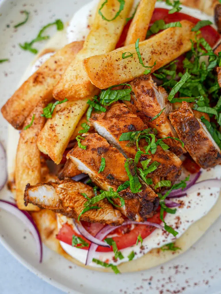A close-up of Chicken Shawarma served with garlic yogurt sauce, garnished with fresh parsley and onions