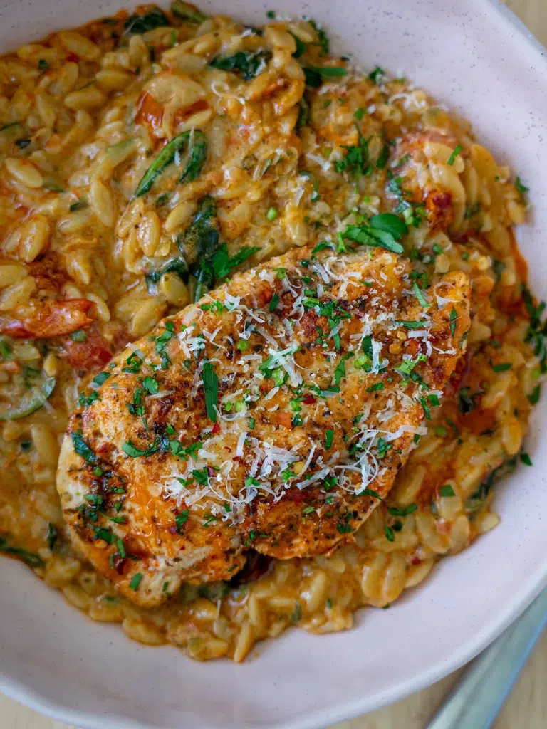 Close-up of chicken with creamy red pesto risoni on a serving plate.