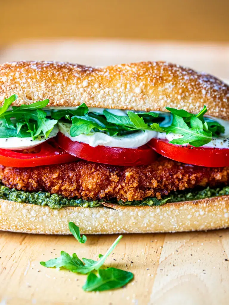 Close-up of crispy chicken pesto sandwich with layers of chicken, pesto, and melted cheese