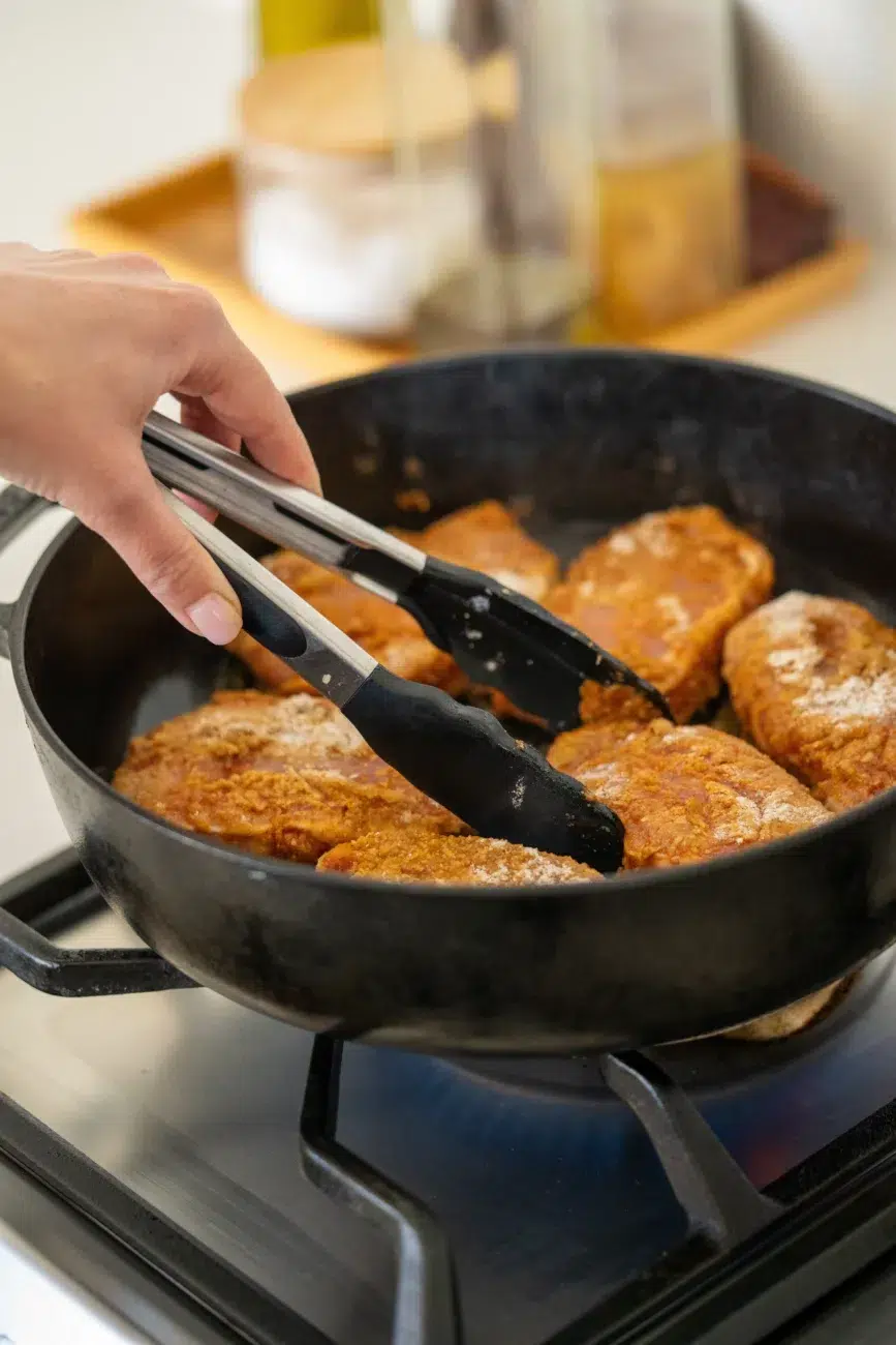 Hand using tongs to sear seasoned pork chops in a cast iron skillet on the stovetop