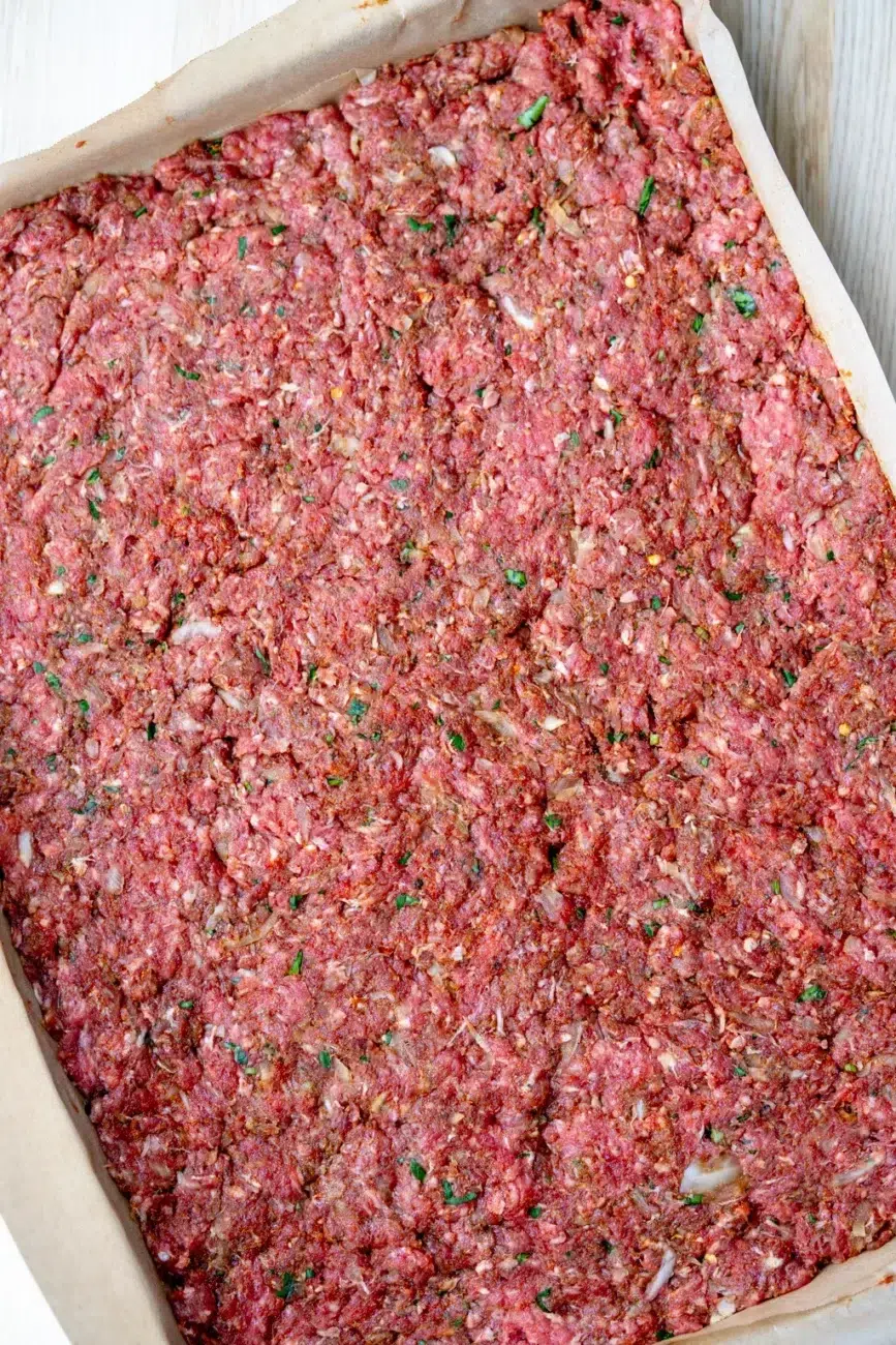 Spiced ground meat mixture pressed flat in a parchment-lined baking tray, ready for oven-baked kebabs