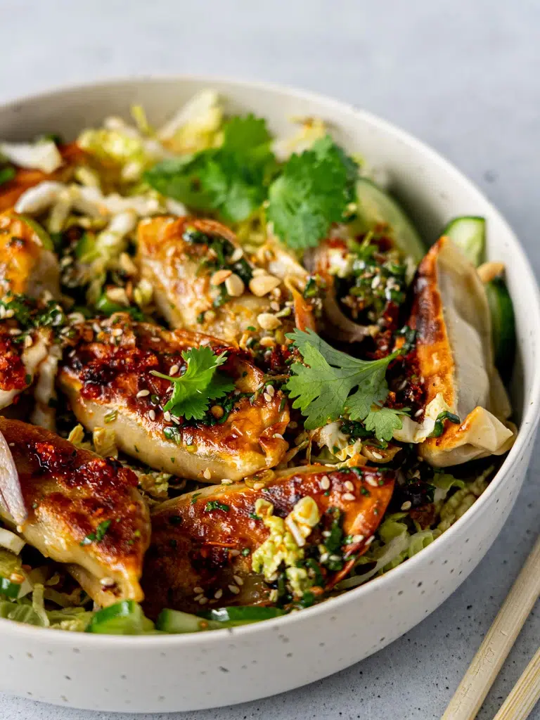 Sesame-Soy Dumpling Salad served with fresh greens, dumplings, and chopsticks placed on the side.