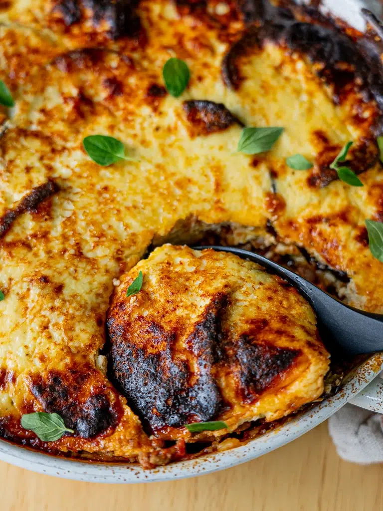 Freshly baked moussaka being served, highlighting its golden topping.