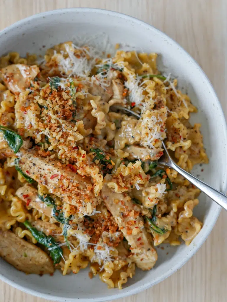 Creamy Parmesan chicken pasta plated with a spoon and herb garnish