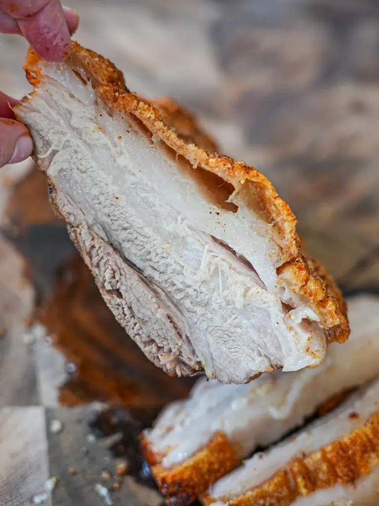 Hand presenting a succulent piece of pork with a golden-brown crust.
