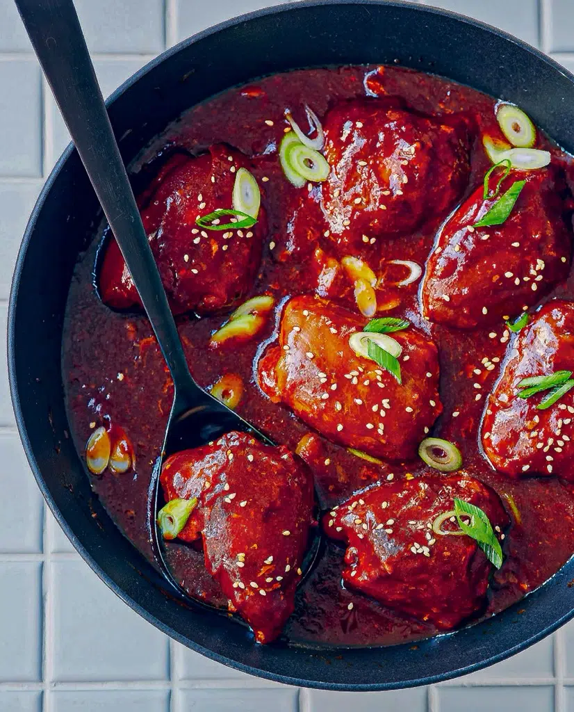 Slow cooker honey garlic chicken served in a pan, topped with fresh spring onions