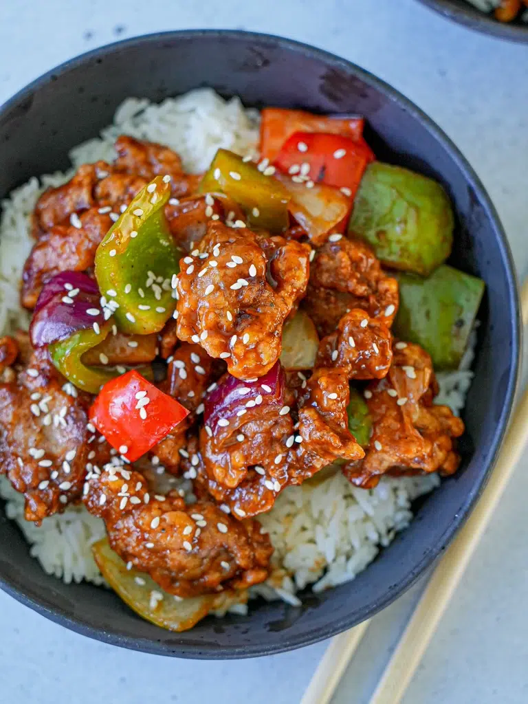 Sweet and sour pork dish featuring vibrant bell peppers and a glossy sauce, served in a bowl